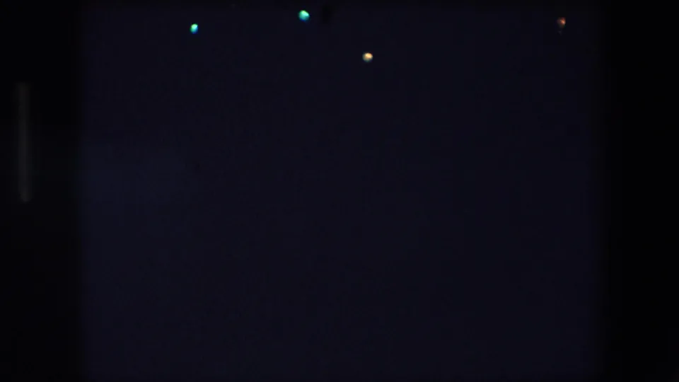 1971 Barcelona 8mm frame with sparse colored points of light in a dark night sky and pronounced grain from the film scan.