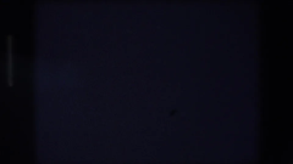 Very dark 1971 Barcelona home-movie frame with scattered distant lights and little visible structure beyond the low-light urban scene.