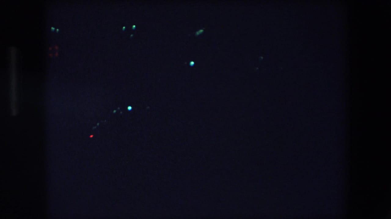 Dark night view with several small blue-white lights and a few red points in the distance.
