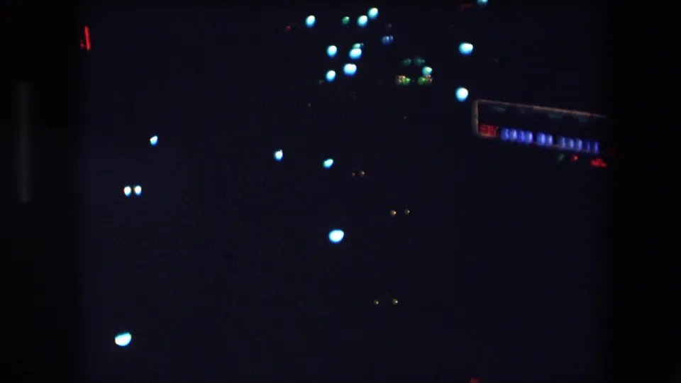 1971 Barcelona 8mm night footage showing scattered blue-white and amber light flares against a mostly black urban scene.