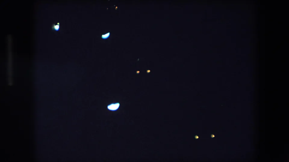 1971 Barcelona night frame with a faint rectangular illuminated display near the upper left and isolated light flares across the darkness.