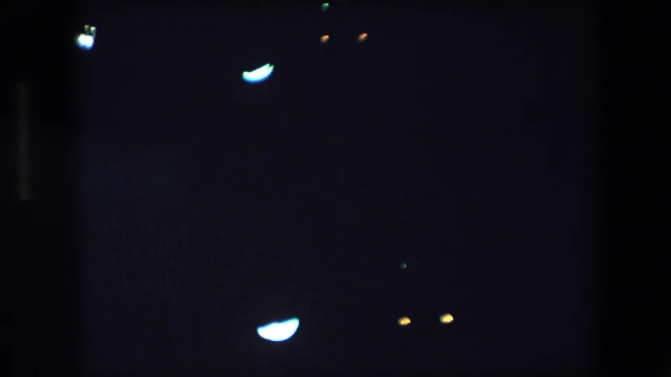 1971 Barcelona 8mm frame with a bright curved blue-white light flare, small amber points, and deep underexposed darkness.