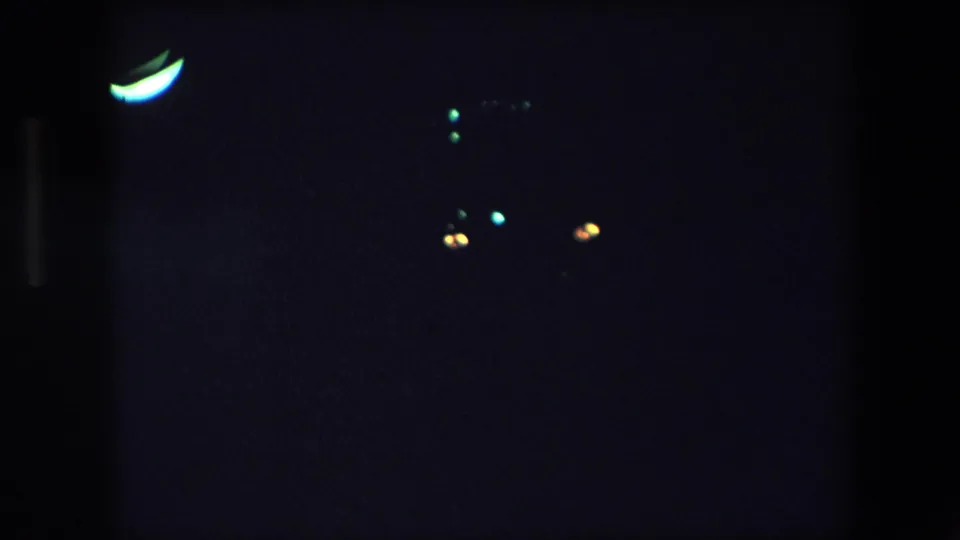 1971 Barcelona night footage frame with sparse blue and amber points of light in a mostly black underexposed scene.