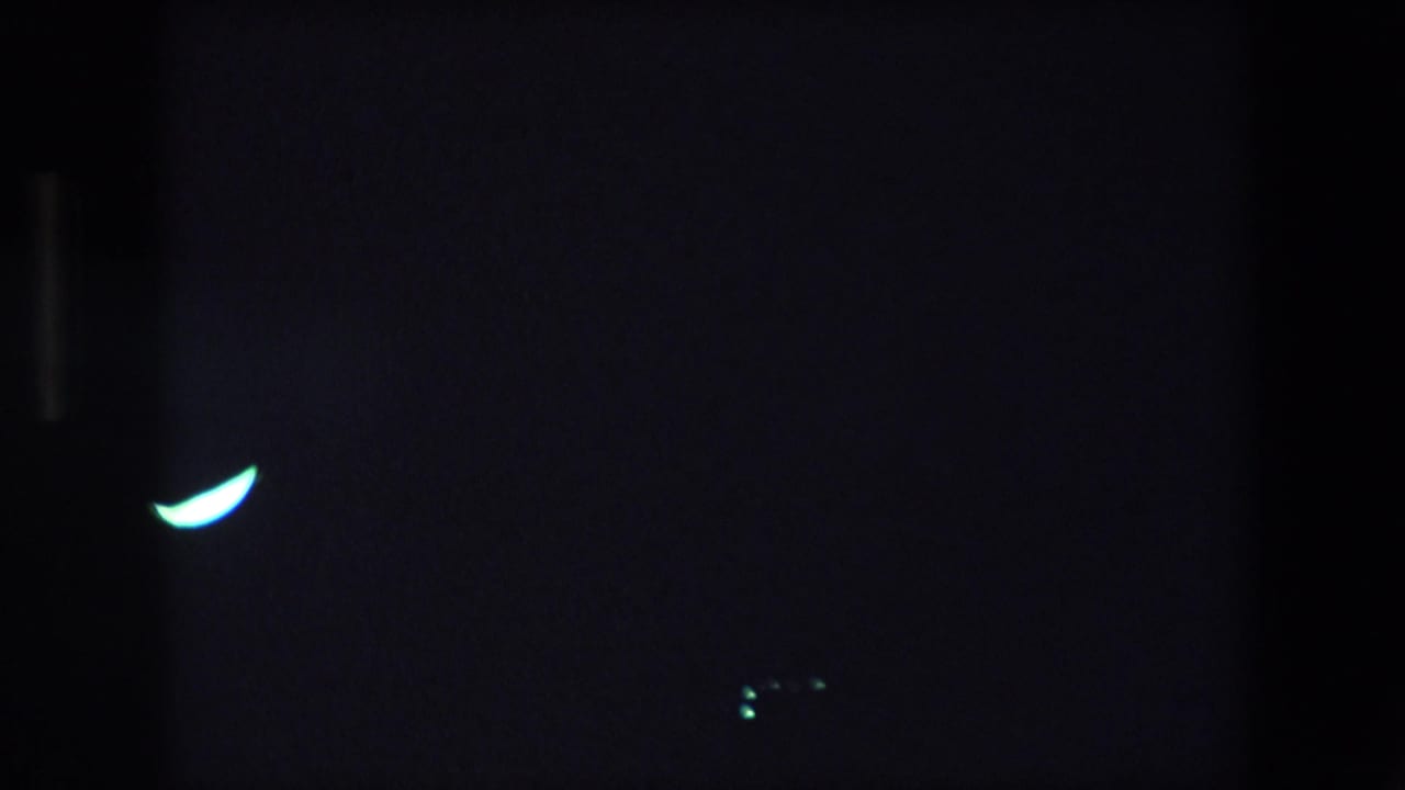 Dark frame with a bright crescent-shaped light near center and faint vertical shadowing.