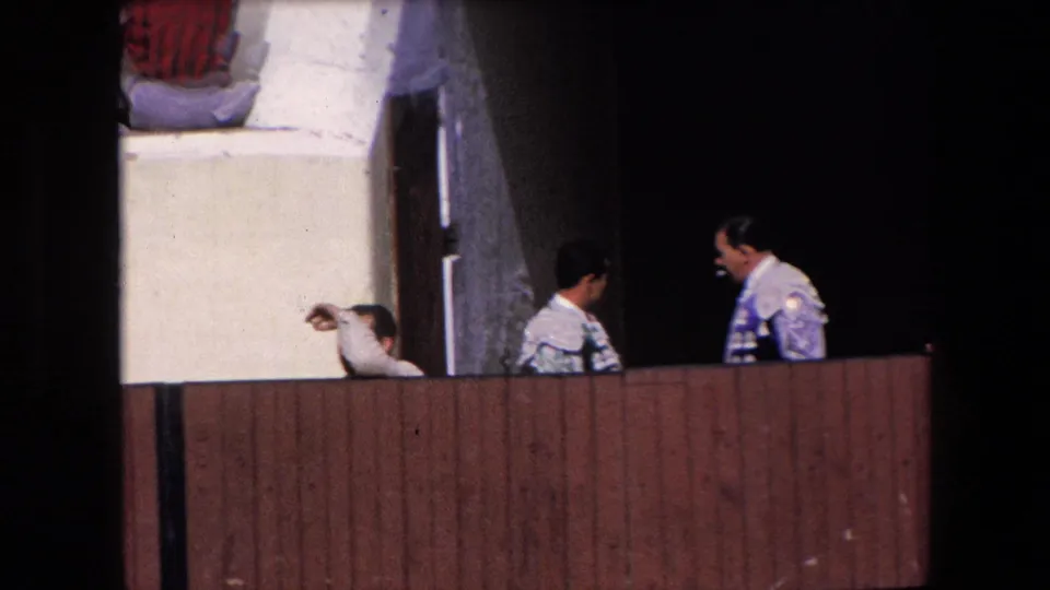 Two matadors in ornate light-colored suits stand and converse near a dark bullring entrance in 1971 Barcelona.