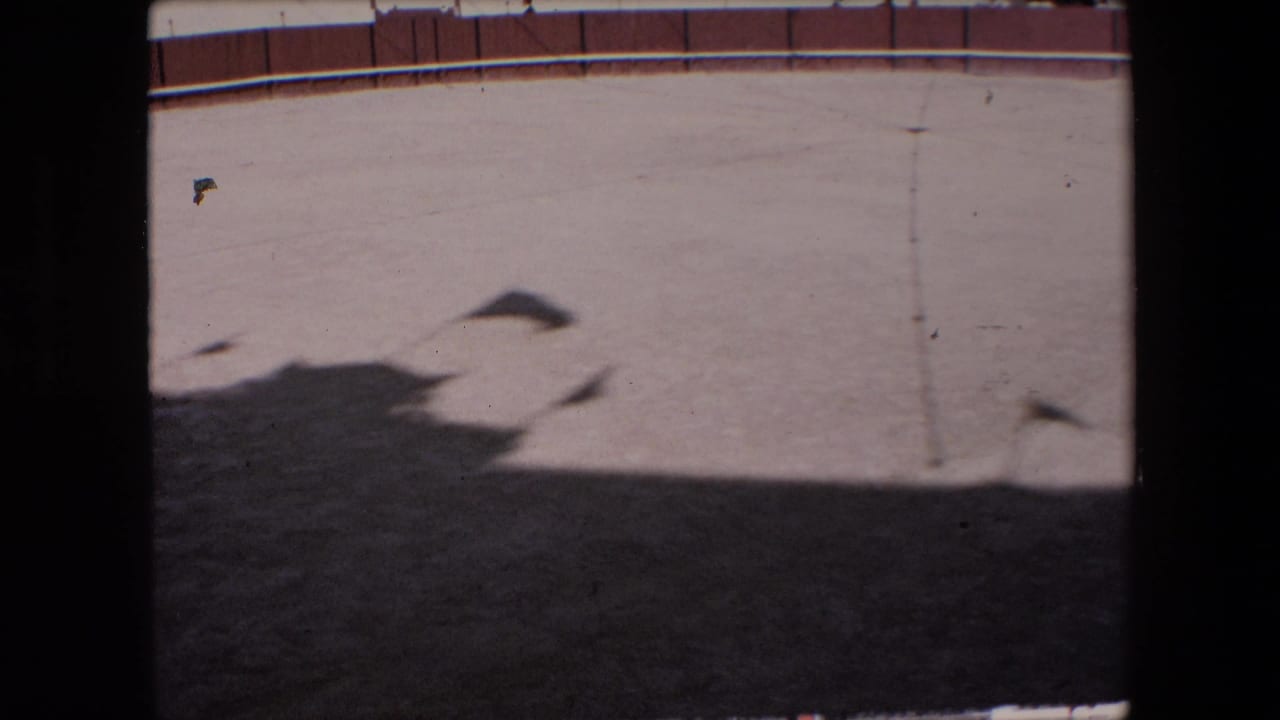 Barcelona 1971 8mm frame showing an empty sandy circular arena from a high viewpoint, with a red-and-white perimeter wall, dark shadow across the foreground, and a vertical obstruction at the side.