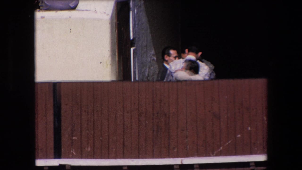 Barcelona 1971 frame showing several men, including a figure in ornate bullfighting attire, standing behind the wooden barrier near a shadowed arena entrance.