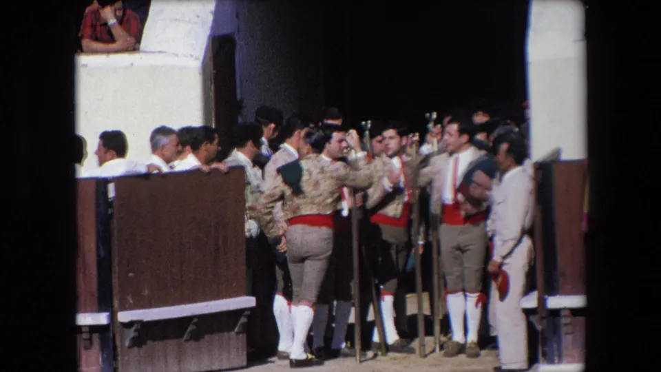 The 1971 Barcelona home-movie frame shows matadors in traditional dress grouped at the bullring entrance, with staffs upright and the dark gate opening behind them.