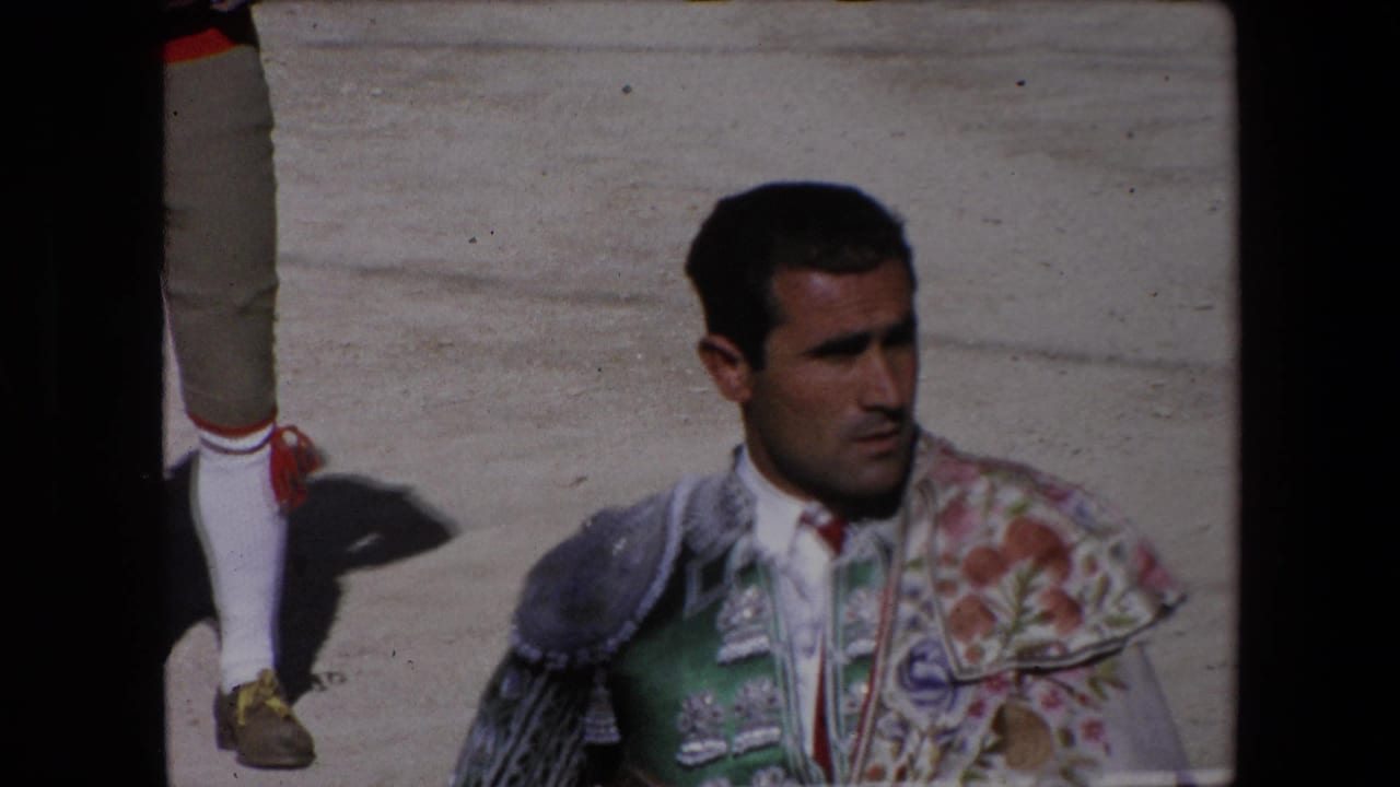 Adult torero in green and floral embroidered bullfighting attire stands in bright sun on arena sand in 1971 Barcelona footage, with another participant partly visible at the edge.