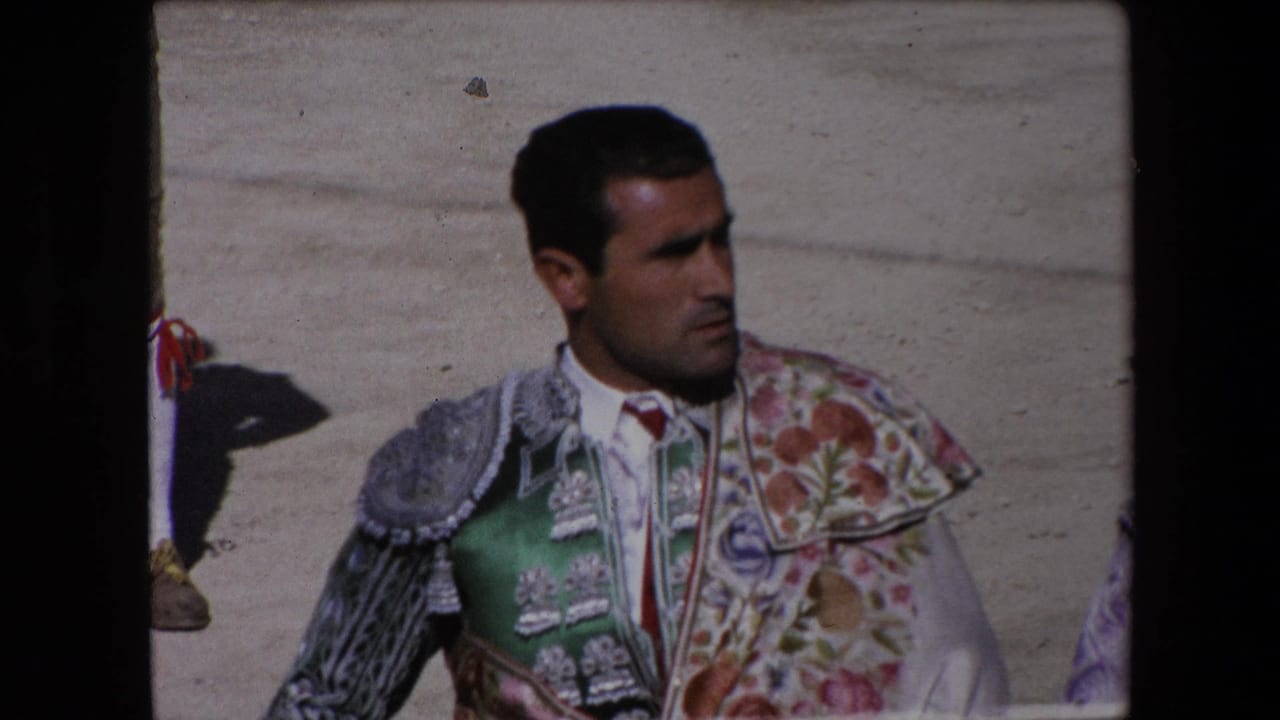 In the Barcelona 1971 home-movie frame, an adult torero in a green suit of lights looks to the side while standing on the sandy bullring floor.