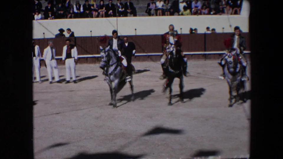 Three riders on decorated horses cross the sandy Barcelona arena as spectators watch from behind the barrier in this 1971 8mm home-movie frame.