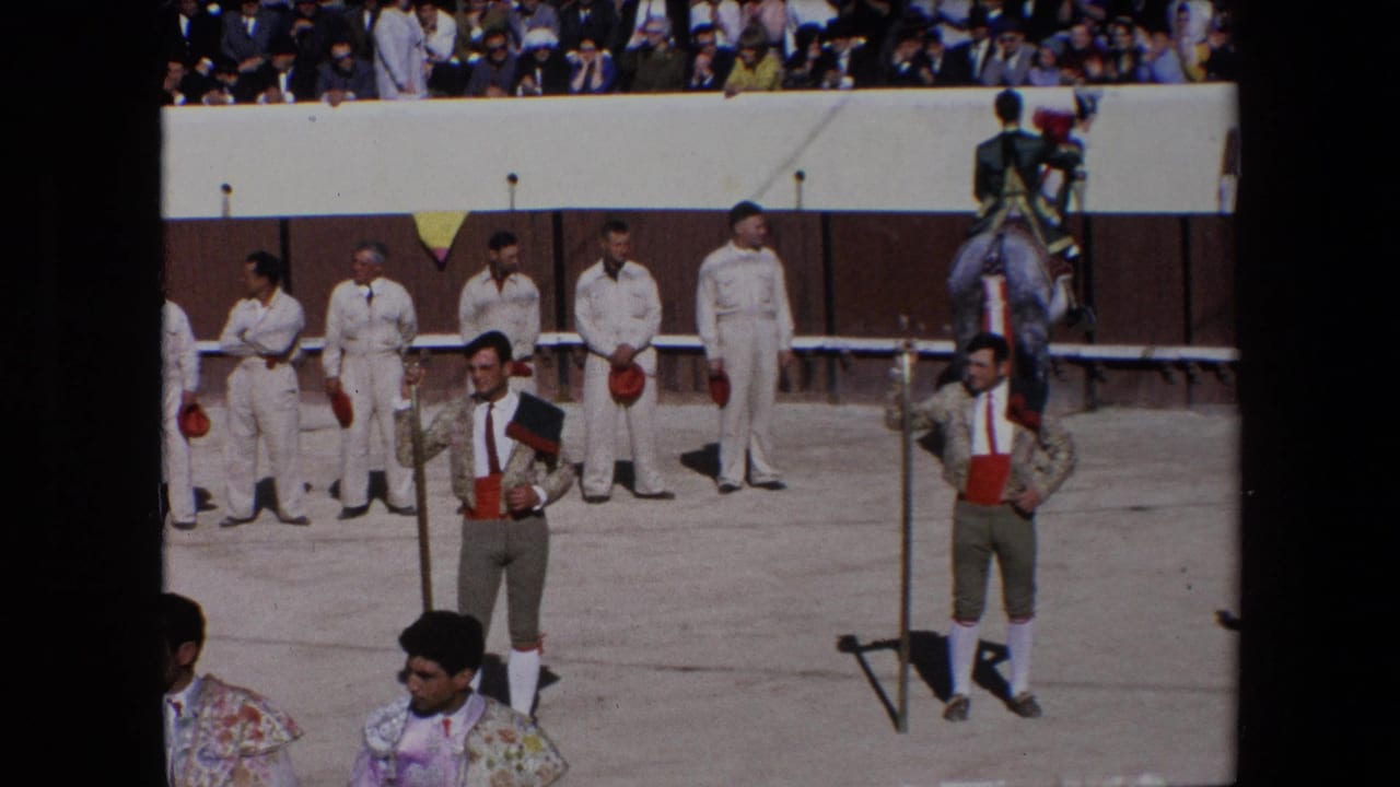 Bullfighter stands near arena staff with spectators watching from the stands.