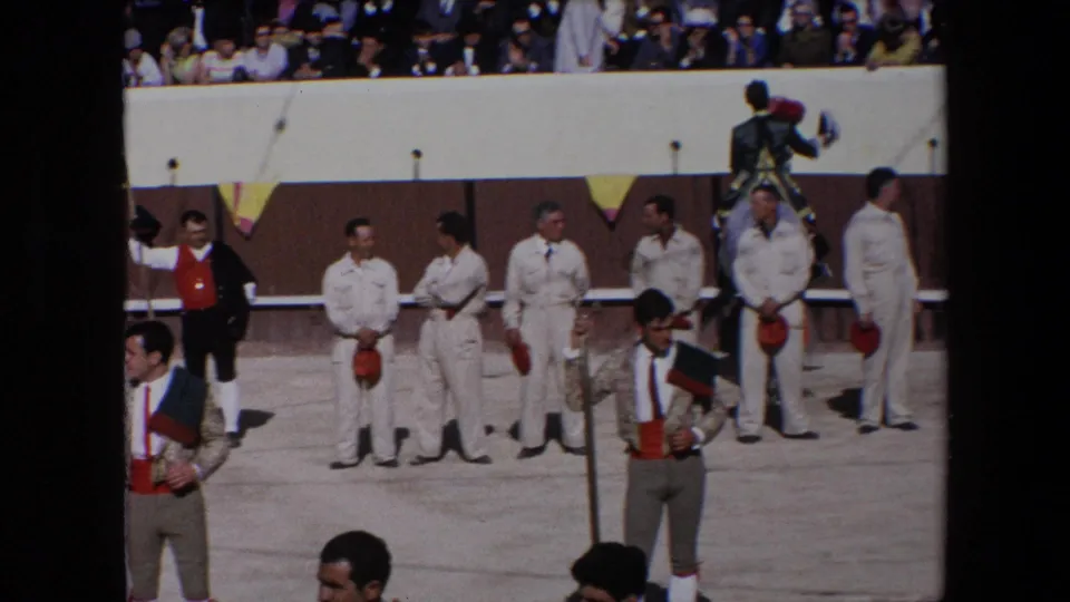 1971 Barcelona bullfighting arena frame with white-uniformed attendants lined by the barrier, bullfighters in decorated jackets, spectators above, and a mounted participant near the right.
