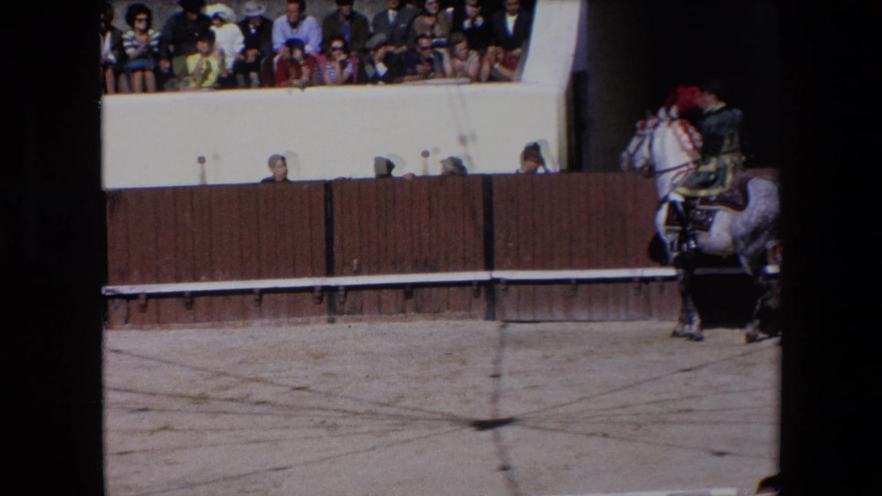 1971 Barcelona 8mm frame showing a rider on a decorated white horse near the wooden barrier of a bullfighting ring, with spectators visible in the upper stands.