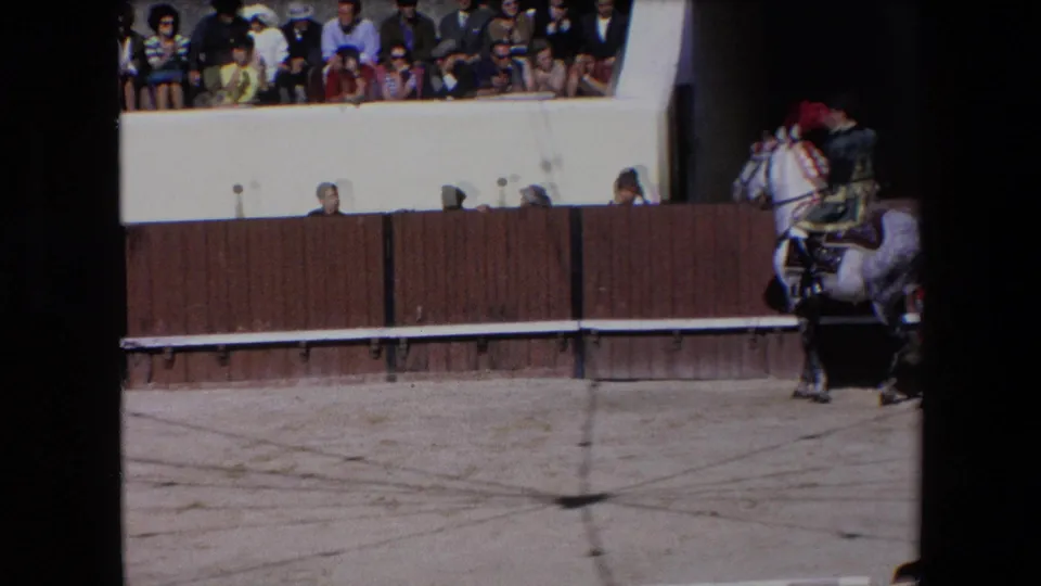 1971 Barcelona 8mm frame showing a rider on a decorated white horse near the wooden barrier of a bullfighting ring, with spectators visible in the upper stands.