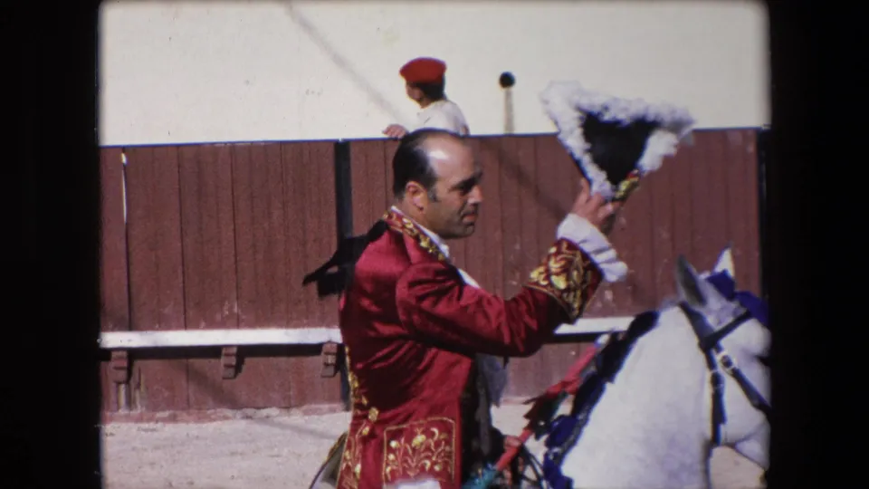 The 1971 Barcelona arena footage shows a red-jacketed mounted participant raising a feathered ceremonial hat beside a white horse, with the wooden ring barrier behind him.