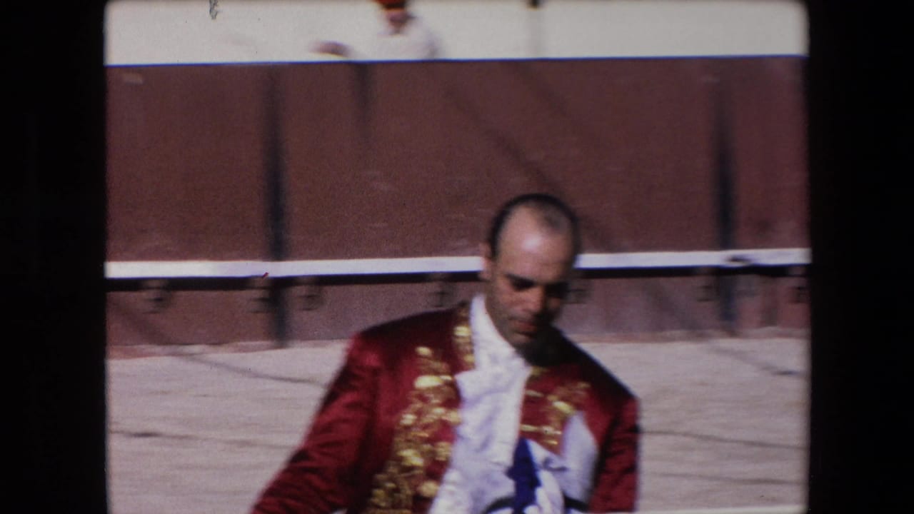 Closer view of the matador in red costume moving past the arena fence.