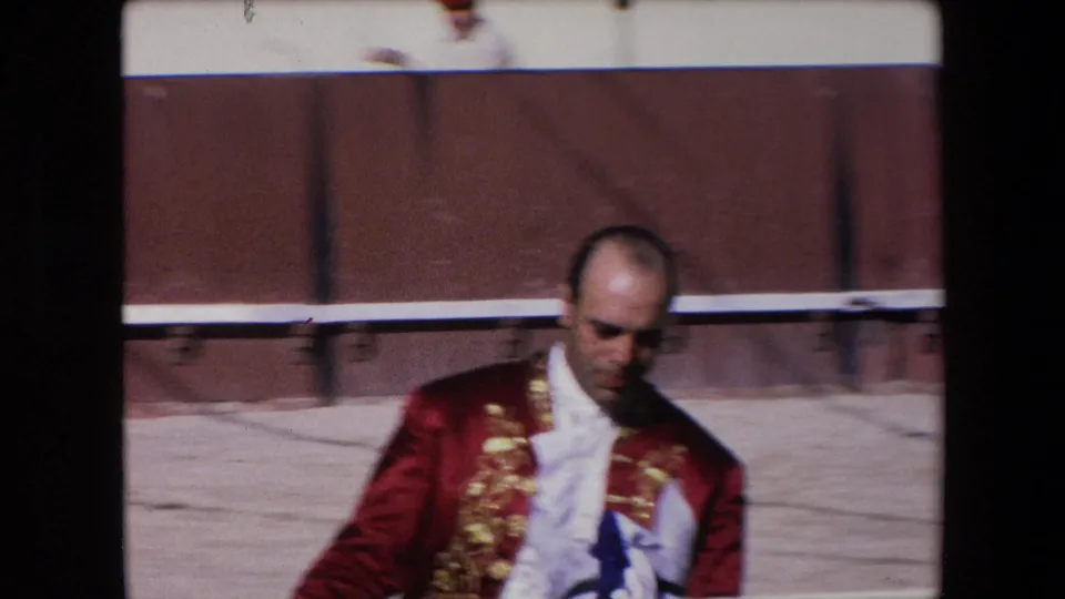 A closer 1971 Barcelona frame shows the matador in a red embroidered jacket and white shirt passing in front of the wooden bullring barrier, with spectators partly visible above it.