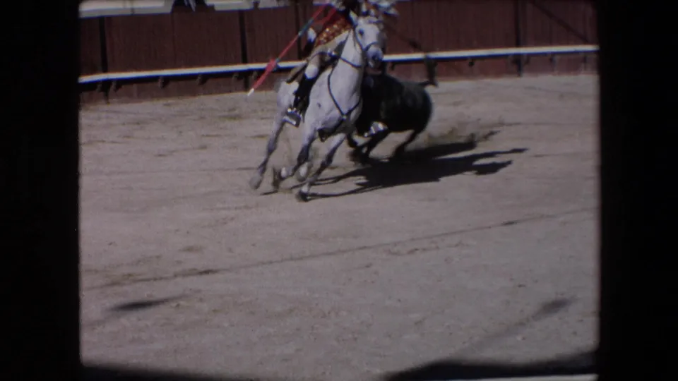 A rider on a white horse turns near a black bull in the sandy ring, with arena wall and shadows visible in the 1971 Barcelona footage.