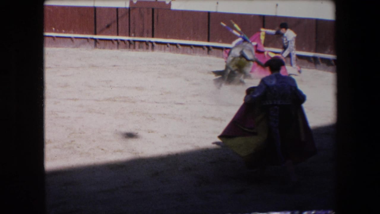 A matador with a dark cape stands in the foreground as a bull moves near a colorful cloth and another suited figure in the 1971 Barcelona arena.