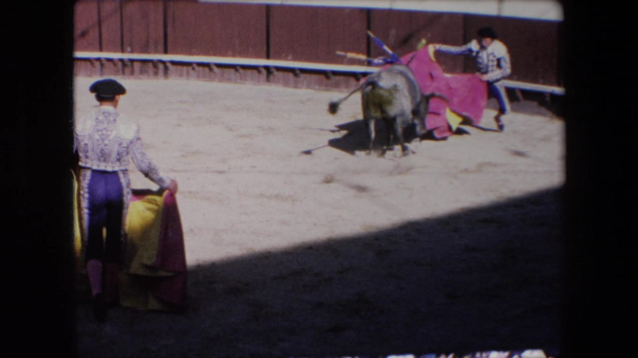 A foreground matador holding a red and yellow cape watches another matador engage the bull across the sandy Barcelona arena.