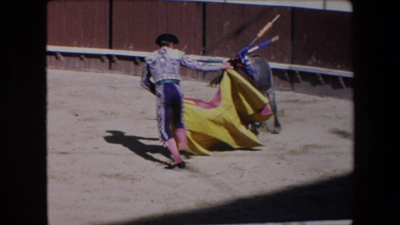 In supported 1971 Barcelona footage, a matador in ornate dress holds a red and yellow cape as a black bull approaches across the sunlit arena.