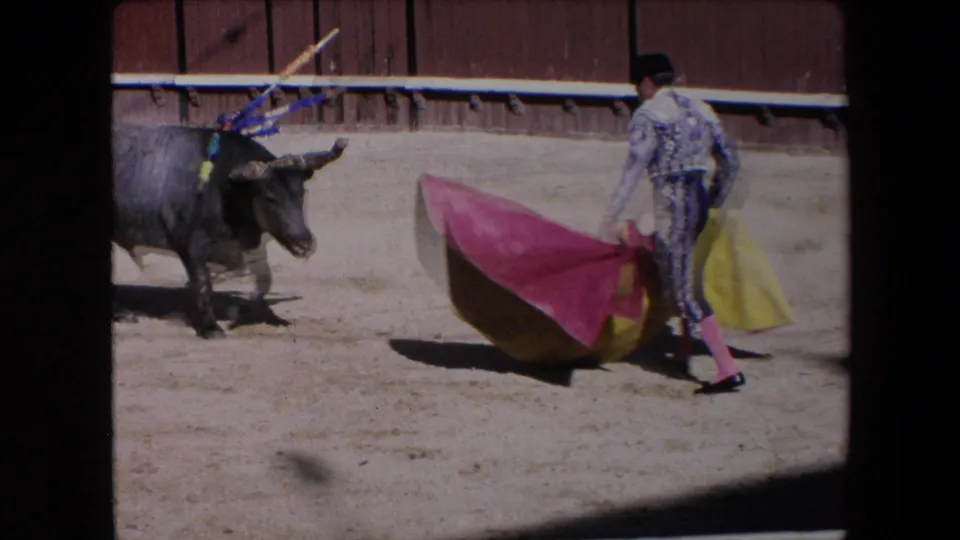 The 1971 Barcelona bullfighting footage shows the matador repositioning the red and yellow cape while the bull faces him from the left side of the sandy ring.