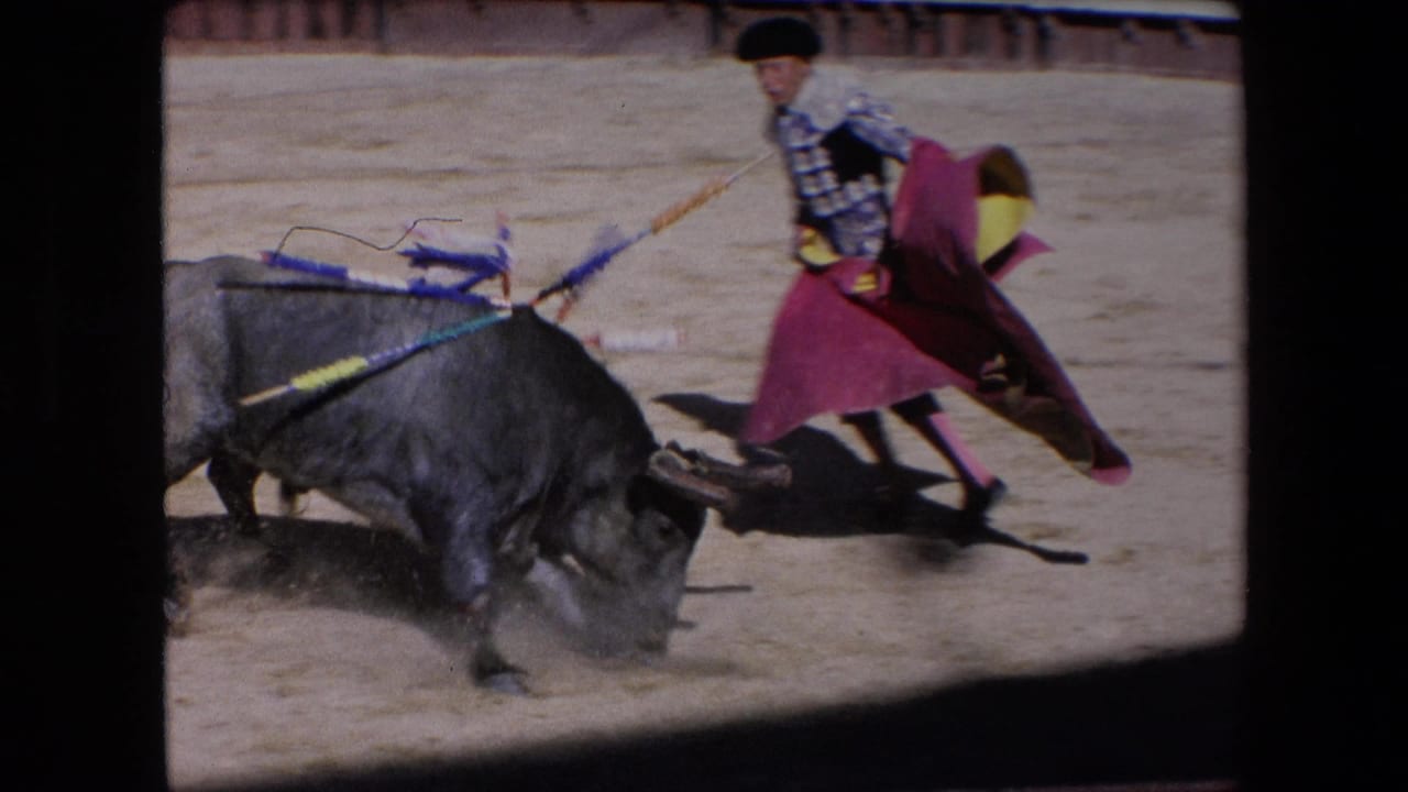 In a 1971 Barcelona bullfighting scene, a dark bull lowers its horns toward a matador in a silver and blue suit holding a red and yellow cape.