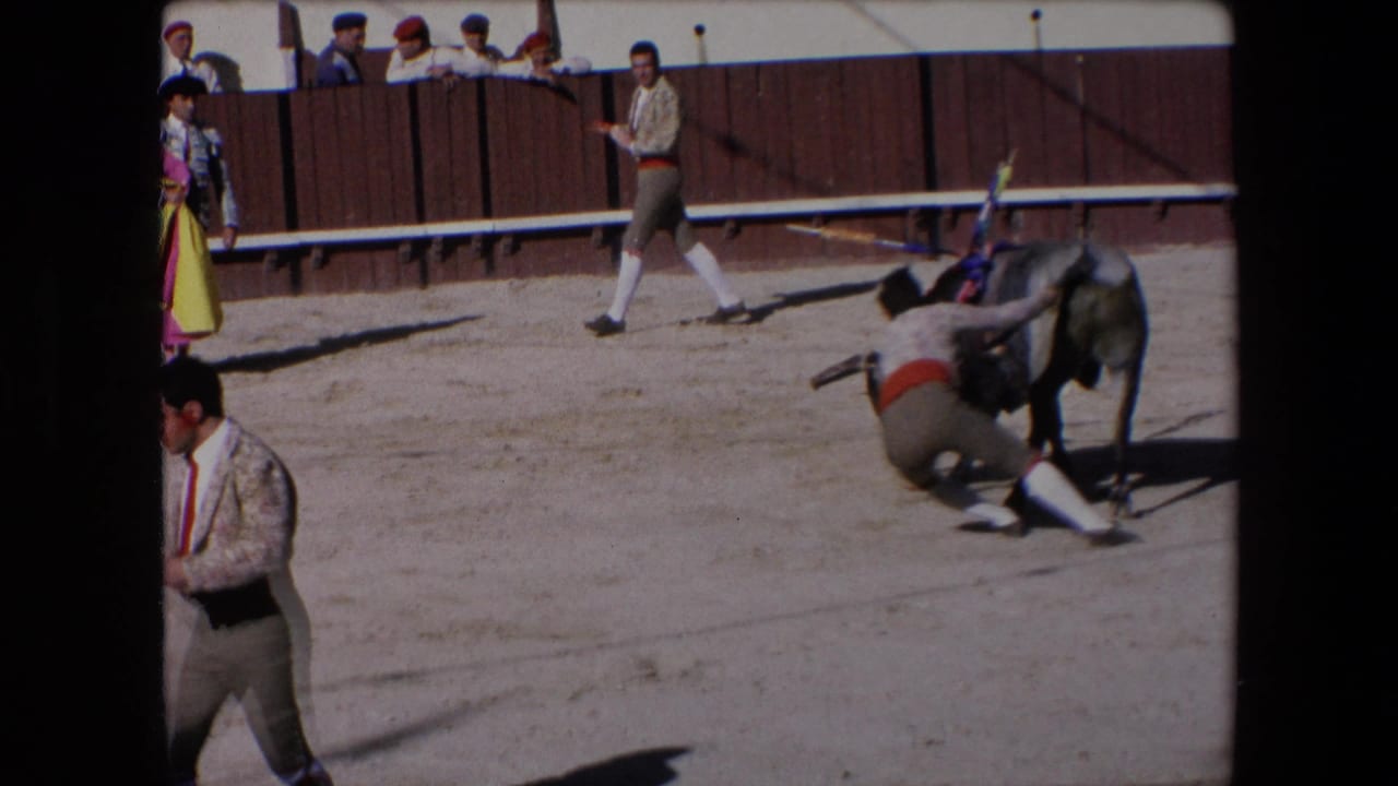 Barcelona, Spain, 1971 8mm frame showing a grey bull moving away while a costumed participant is low to the ground near the bull's hind legs.