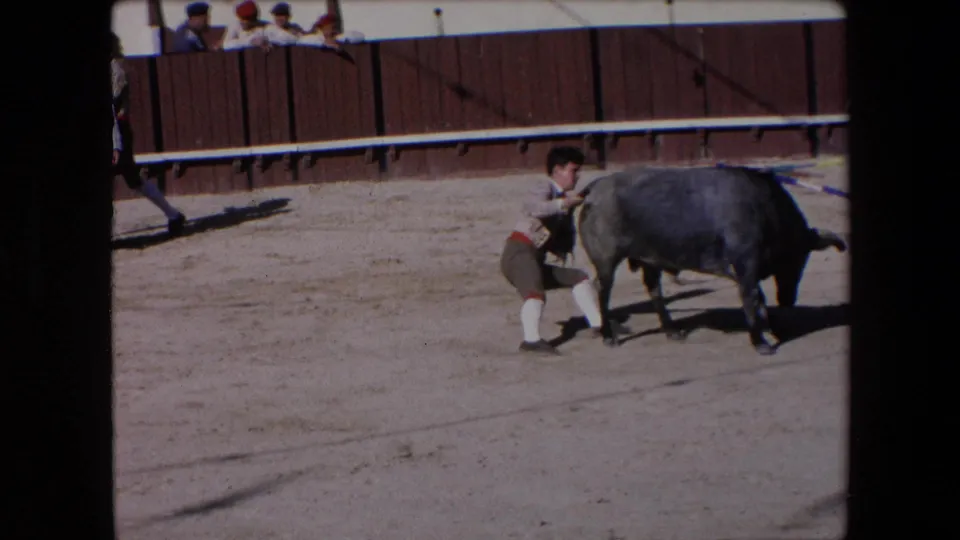 Barcelona, Spain, 1971 8mm frame showing a costumed bullfighting participant close to a grey bull near the center of a sandy arena.