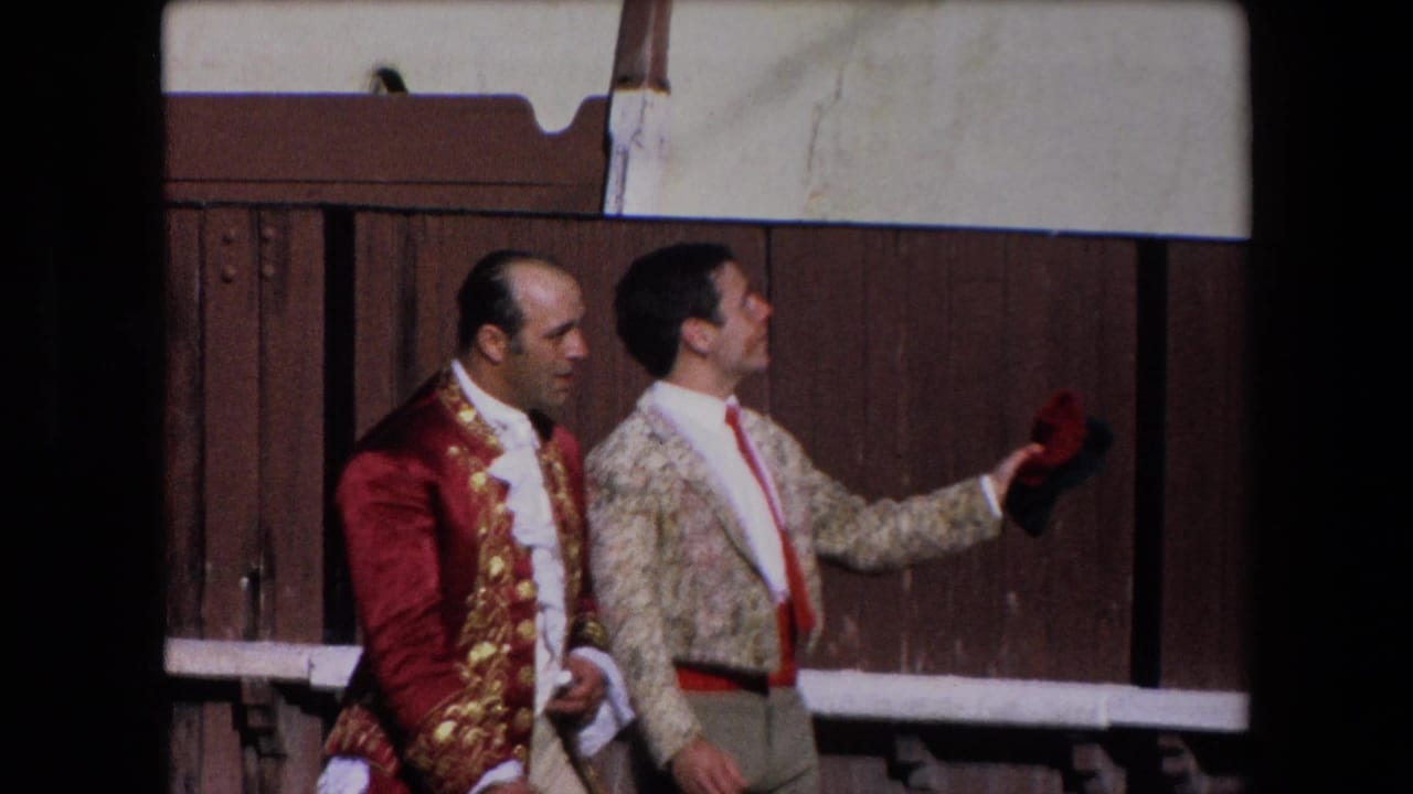 Two bullfighters in ornate jackets stand beside the wooden barrier in the 1971 Barcelona arena, with one holding a small red cap or cloth.