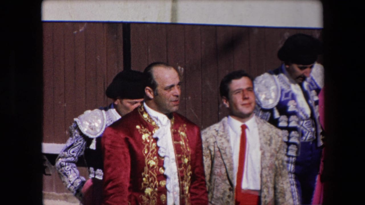 A small group of bullfighters in ornate red, gold, blue, and white costumes stand near the wooden barrier during the 1971 Barcelona bullfighting event.