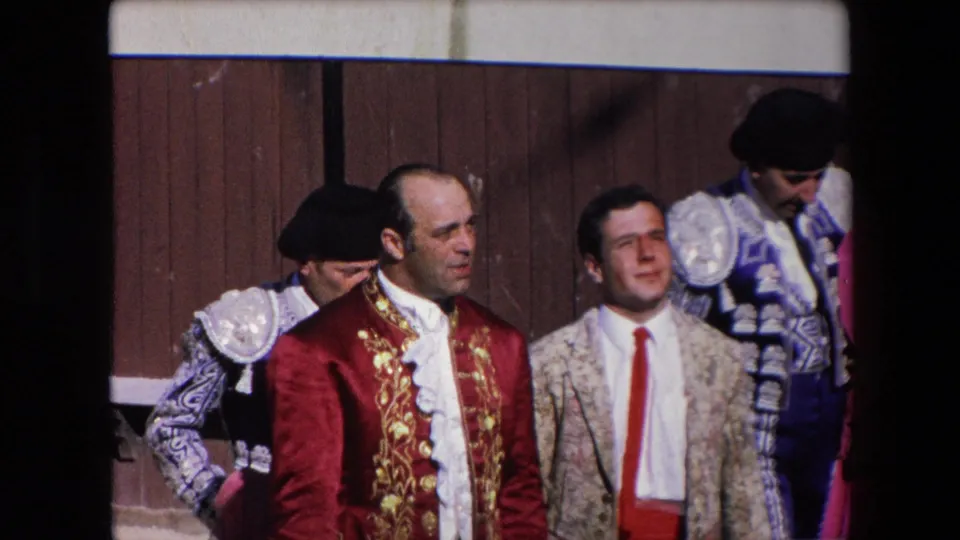 A small group of bullfighters in ornate red, gold, blue, and white costumes stand near the wooden barrier during the 1971 Barcelona bullfighting event.