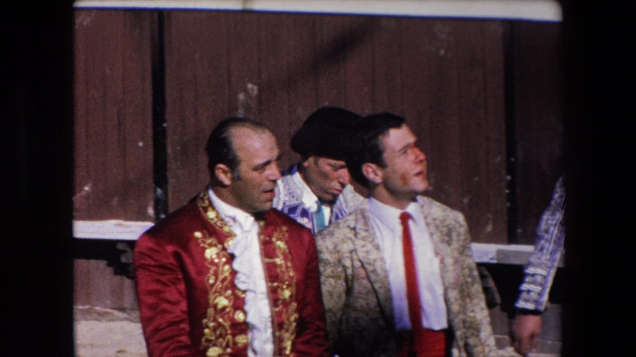 In Barcelona, Spain in 1971, several men including a matador in a red-and-gold jacket walk past a wooden enclosure in a bullring or stadium setting.