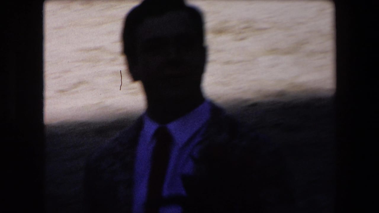 A dark silhouetted man stands against a sandy background.