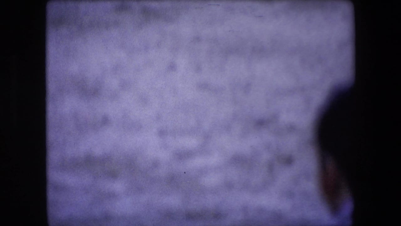Soft-focus 1971 Barcelona home-movie frame showing a partially seen spectator or passerby against a pale arena-like wall, divided by dark film-frame borders.