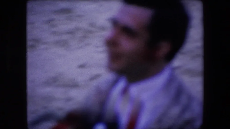 Blurred 1971 Barcelona frame of a man in a light shirt standing near a pale wall, with the home-movie focus drifting away from his face.