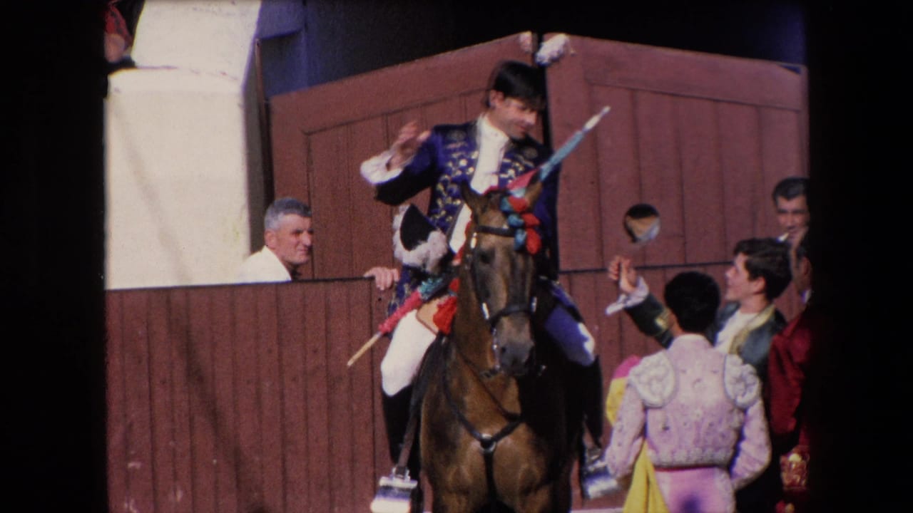 The mounted performer in blue and gold raises his hand while a brown horse stands at the open wooden gate, with costumed figures and onlookers visible around the entrance.