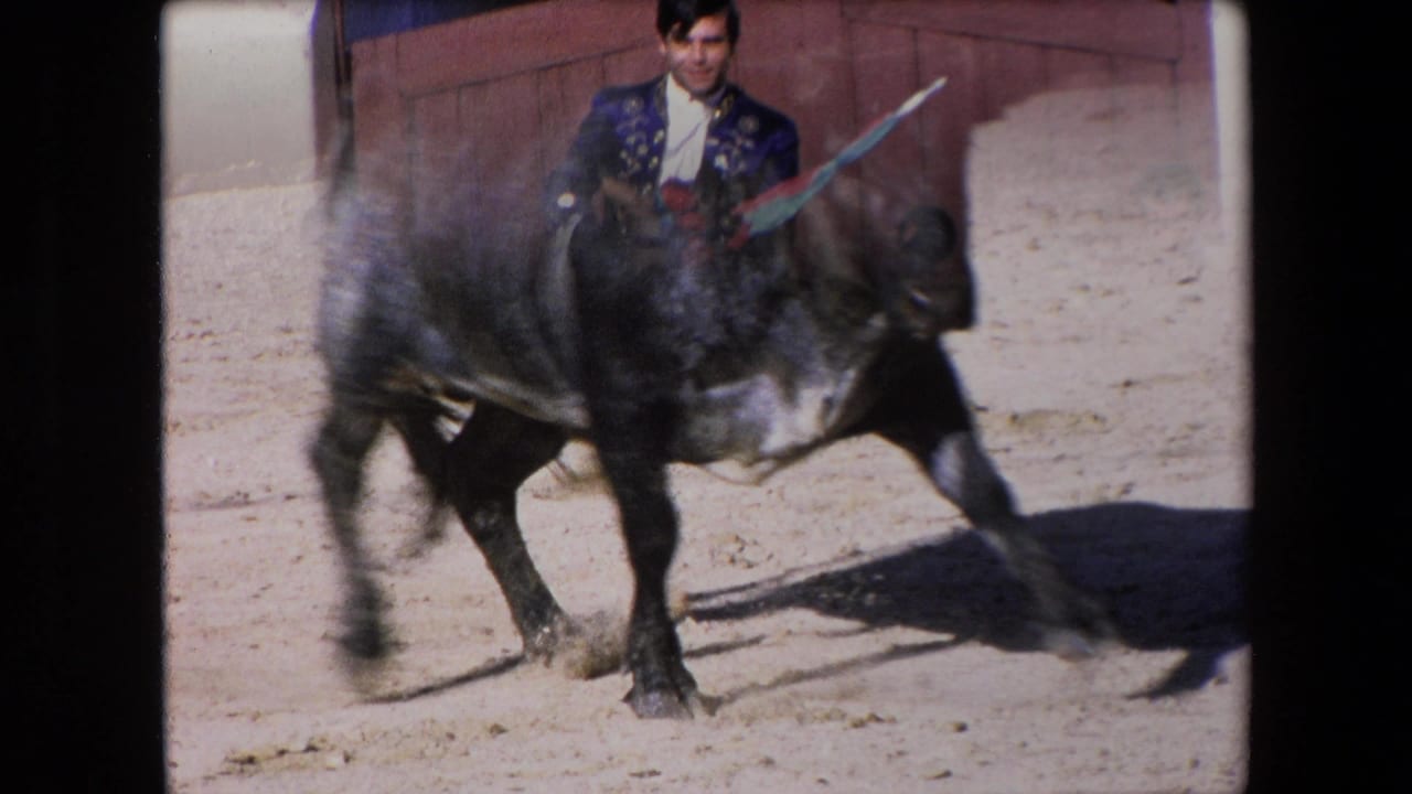 In 1971 Barcelona 8mm footage, a costumed mounted bullfighting performer rides near a dark bull in a sandy arena with wooden boards behind them.