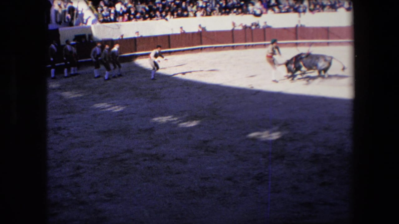 A wider 8mm view shows the bull, multiple arena figures, capes, and a crowded spectator section during the Barcelona bullfight identified in the clip metadata.