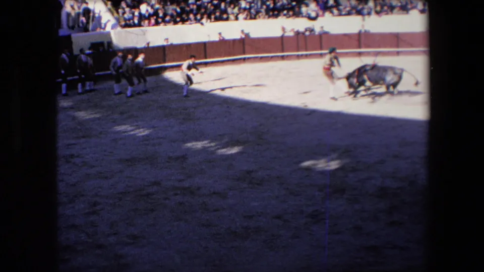 A wider 8mm view shows the bull, multiple arena figures, capes, and a crowded spectator section during the Barcelona bullfight identified in the clip metadata.