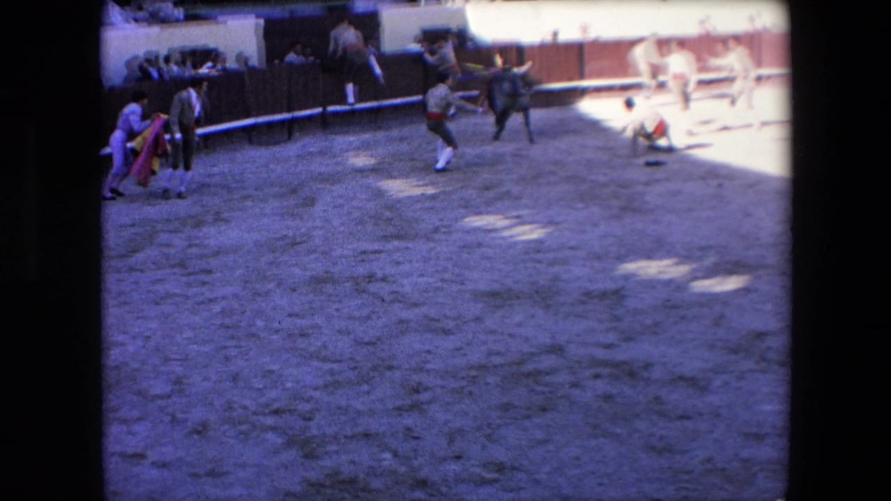 1971 Barcelona bullring footage from an elevated spectator view, showing people in the sandy arena near a dark bull with the crowd and barrier beyond.