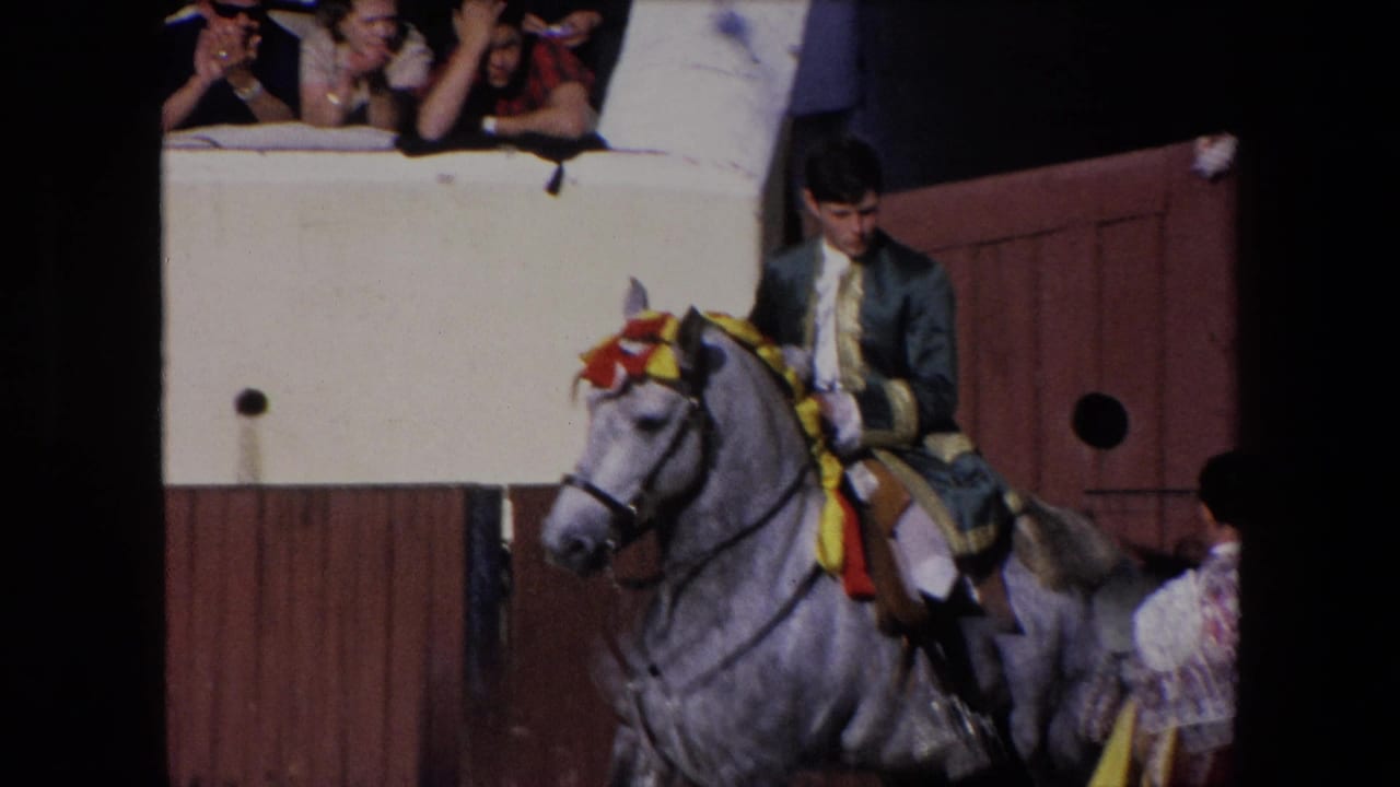 The rider appears to steady or guide the decorated grey horse as it moves along the wooden pen in the 1971 Barcelona home-movie footage, while spectators watch from the raised edge.