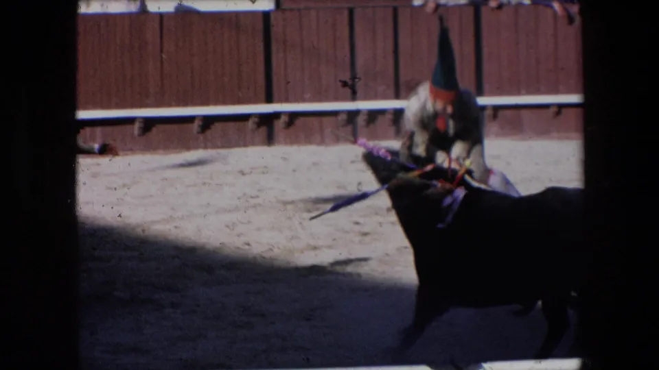 The bullfighter appears close to the black bull near the wooden arena boards, with the figure partly bent forward and the 8mm image showing motion softness.