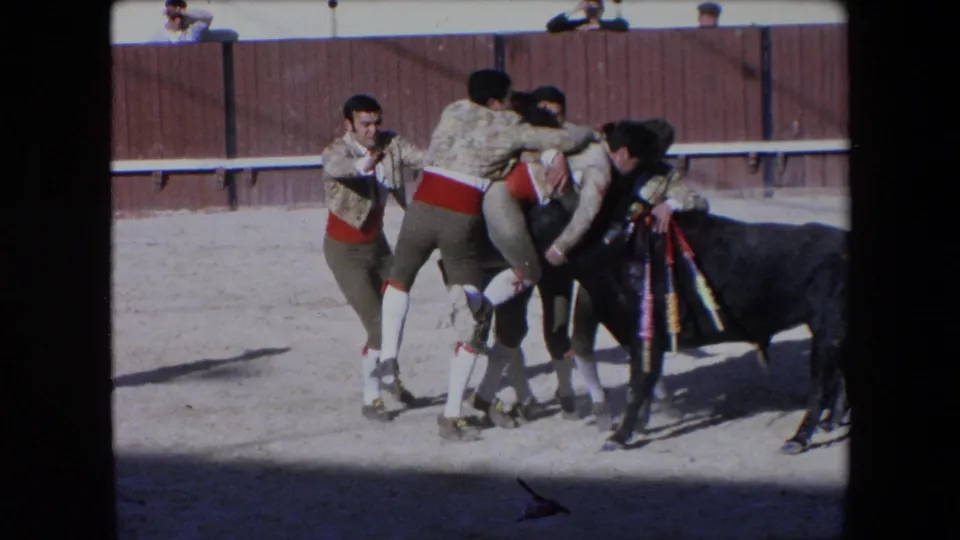 In the Barcelona bullfight scene, several costumed men cluster near the black bull as one participant appears pressed close to the animal at the edge of the action.