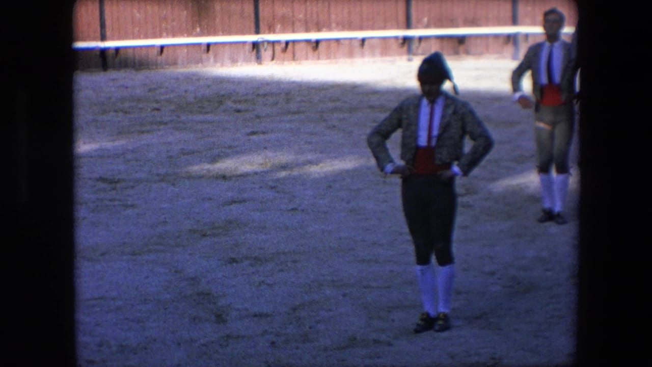 In a 1971 Barcelona bullfighting scene, a matador in traditional costume stands with hands at his waist on a sandy arena floor while another performer waits behind him.