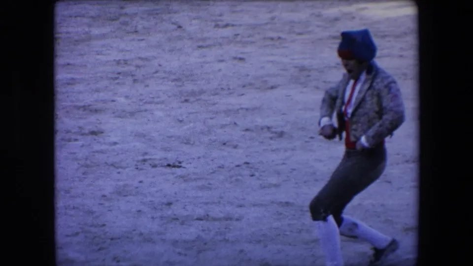 A bullfighter in a patterned jacket, red sash, dark trousers, white stockings, and dark head covering moves across the sandy arena floor in the closing frame.