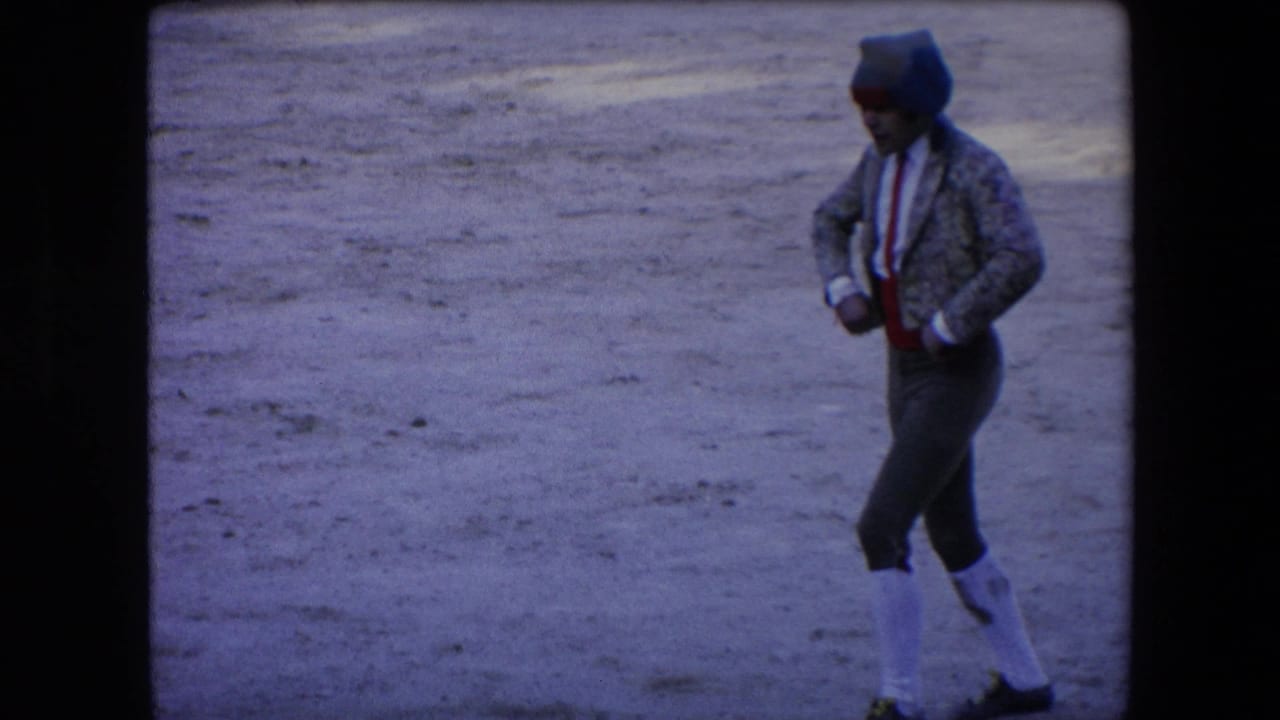 In Barcelona, Spain, in 1971, a matador in patterned jacket, red sash, white stockings, and cap moves across a dusty bullfighting arena.