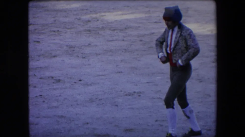 In Barcelona, Spain, in 1971, a matador in patterned jacket, red sash, white stockings, and cap moves across a dusty bullfighting arena.