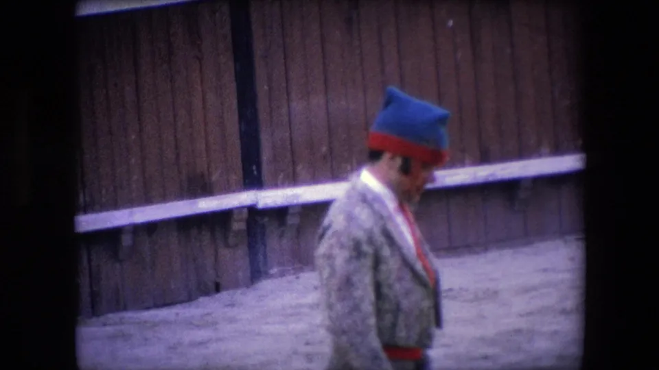 A man in a patterned jacket and blue-and-red hat walks across the sandy arena in the 1971 Barcelona home-movie footage.